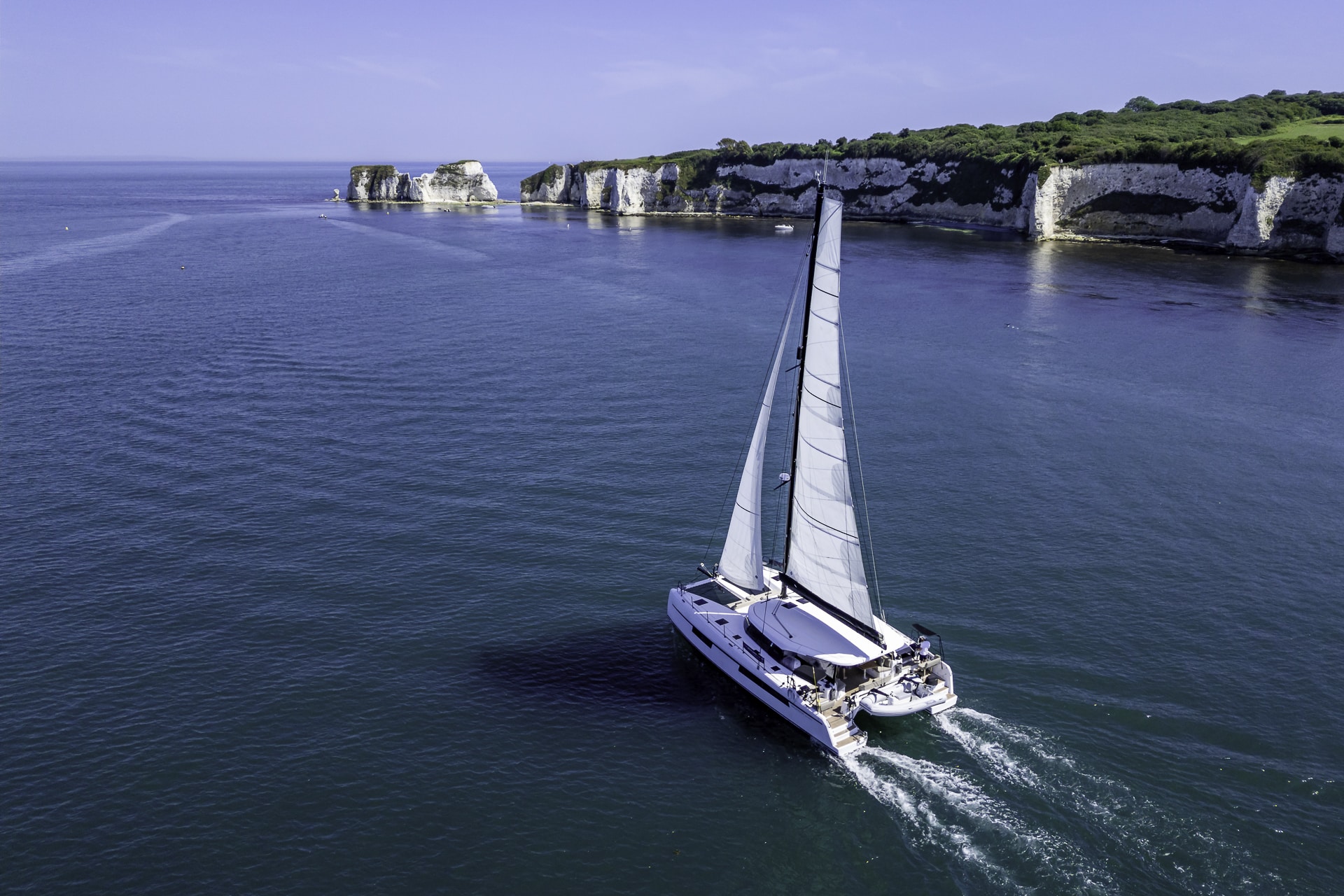 Seven Days luxury catamaran sailing past Old Harry Rocks on the Jurassic Coast during a private yacht charter from Poole Harbour.