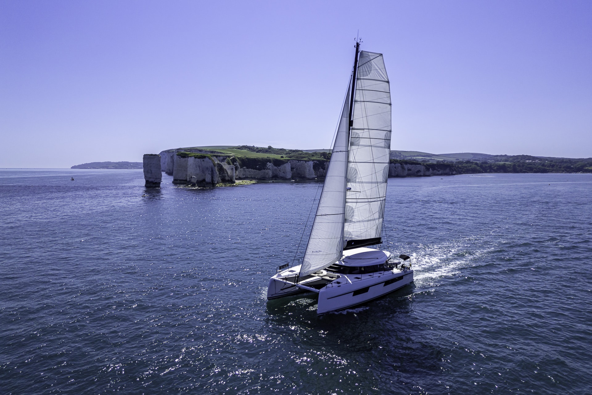 Luxury catamaran under sail near Old Harry Rocks, showcasing the spectacular Jurassic Coast during a private Dorset yacht charter.