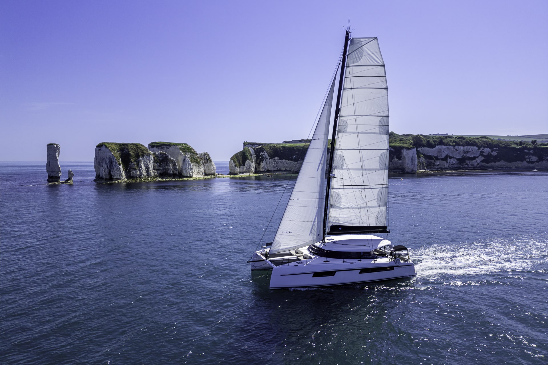 Seven Days luxury catamaran sailing past Old Harry Rocks on the Jurassic Coast, showcasing a private yacht charter experience in Dorset.